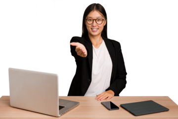 Young business asian woman sitting on a table isolated stretching hand at camera in greeting gesture.