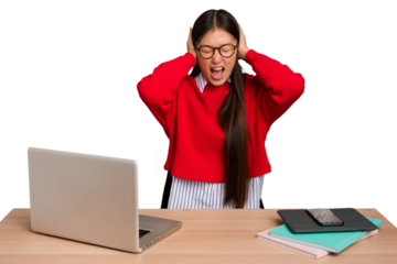 Young student asian woman in a workplace with a laptop isolated covering ears with hands trying not to hear too loud sound.