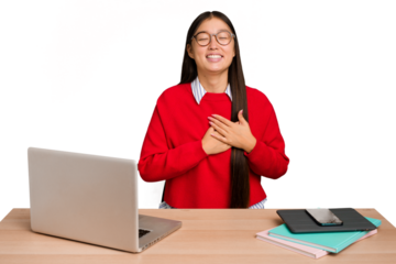 Young student asian woman in a workplace with a laptop isolated laughing keeping hands on heart, concept of happiness.