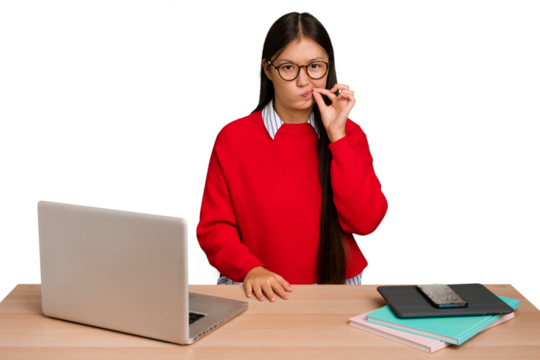 Young student asian woman in a workplace with a laptop isolated with fingers on lips keeping a secret.