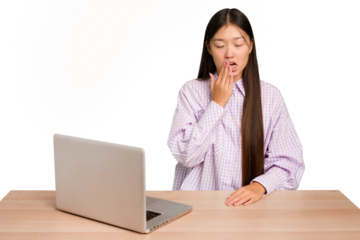 Young student asian woman in a workplace with a laptop isolated yawning showing a tired gesture covering mouth with hand.