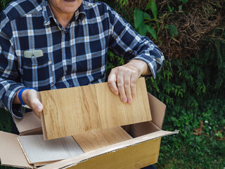 Front view of curios senior male unboxing unpacking parquet wooden floor samples from the cardboard box in green garden