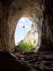 Climber hanging on a rope from a celiling of a giant cave boulder. Climbing in an overhang
