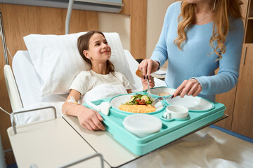 Obraz na płótnie Canvas Mom feeds breakfast to a smiling daughter on hospital bed