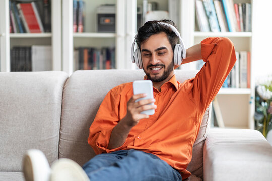 Happy Arab Guy Relaxing On Couch With Phone And Headphones