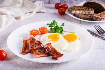 Fried eggs and bacon, tomatoes and parsley on a plate on the table. Homemade breakfast.
