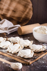 Raw dumplings on a cutting board and flour on the table. Home cooked food. Vertical view