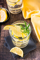 Pieces of lemon in a glass of water and rosemary on a wooden table. Detox drink. Vertical view
