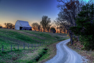 Silent Barn.  A gravel road snakes up a hill to a barn at the top of a hill.  Blue hour light leaves a mauve glow on the horizon. 