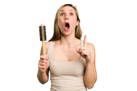 Young caucasian woman using an hair comb isolated pointing upside with opened mouth.