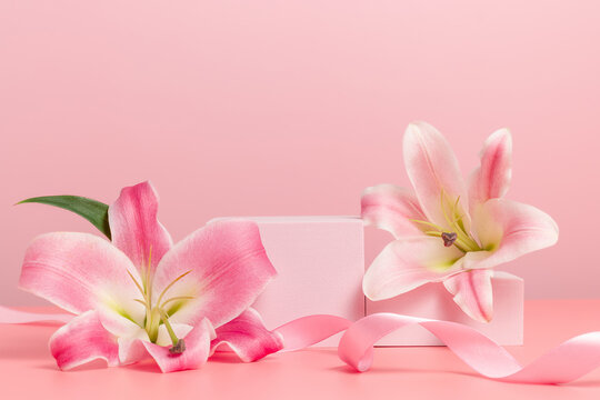 Empty podium with lily flowers and festive ribbon on pink background. Showcase for product, gift, perfume and cosmetic presentation, holidays concept