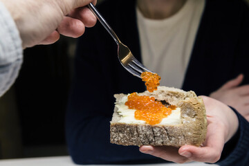 Woman arranging with a fork eating deliciosu Red caviar on the bread with butter - delcision luxury expensive food