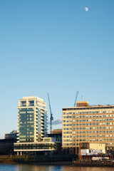 Fototapeta na wymiar Tall building in sunshine with crane in front of river thames in London and moon overhead