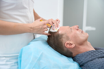 Obraz na płótnie Canvas Aging gentleman having cosmetologist inject skin renewal plasma into face