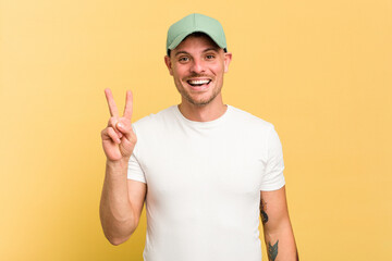 Young caucasian handsome man isolated on yellow background showing victory sign and smiling broadly.
