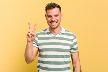 Young caucasian handsome man isolated on yellow background joyful and carefree showing a peace symbol with fingers.