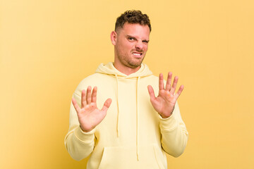 Young caucasian handsome man isolated on yellow background rejecting someone showing a gesture of...