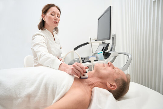 Attentive female doctor examines the thyroid gland of middle-aged man