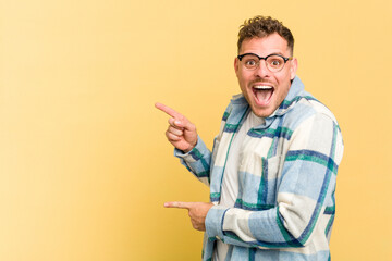 Young caucasian handsome man isolated on yellow background excited pointing with forefingers away.