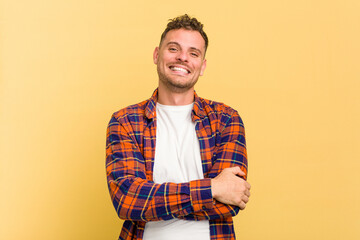 Young caucasian handsome man isolated on yellow background who feels confident, crossing arms with determination.