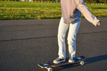 Cropped shot of legs on longboard. Skater girl riding her skateboard on street. Female teenager on...