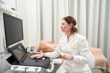 Woman specialist looks at screen of ultrasound machine at her workplace