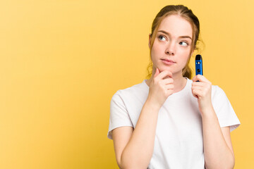 Young cute woman holding a vaper isolated on yellow background looking sideways with doubtful and...