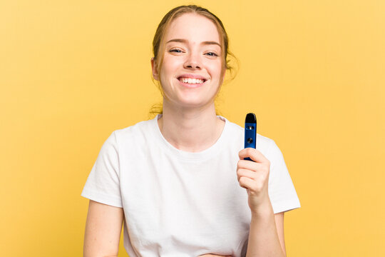 Young cute woman holding a vaper isolated on yellow background laughing and having fun.