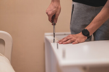 A young man is screwing a screw into a board with a screwdriver.