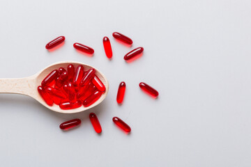 Vitamin capsules in a spoon on a colored background. Pills served as a healthy meal. Red soft gel vitamin supplement capsules on spoon