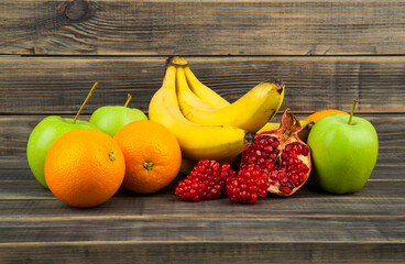 Oranges, apples, pomegranate and bananas on a wooden table.