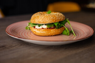 Delicious, yummy sesame donut burger with cheese and greenery filling, sauce served up on pink plate on wooden table