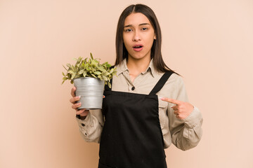 Young colombian gardener woman holding a plant isolated pointing to the side