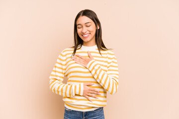Young colombian woman isolated on beige background laughs happily and has fun keeping hands on...