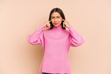 Young colombian woman isolated on beige background covering ears with fingers, stressed and...