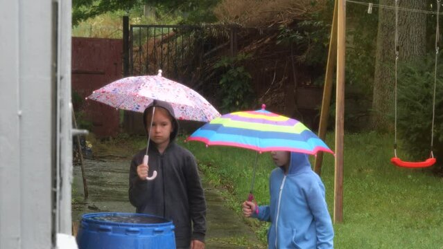 Two elementary school age girls, children walking in the rain with umbrellas. Friends, sisters, siblings outdoors walk on a rainy day Rainy weather, raining outside, slow motion, real people lifestyle