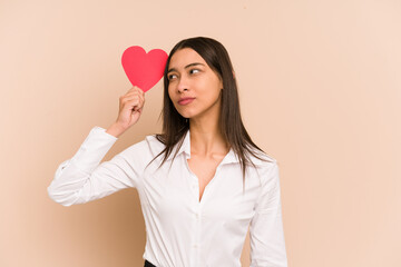 Young colombian woman holding a heart paper for valentines day isolated