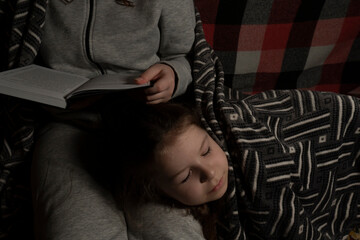 Blackout. Woman in a dark room reading a book to a sleeping little girl