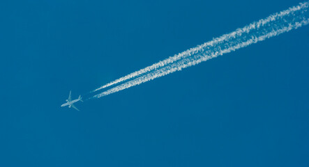 Pasażerski odrzutowiec przecinający błękit nieba , za samolotem potężne smugi kondensacyjne . - obrazy, fototapety, plakaty
