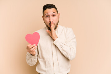 Adult latin man holding a red heart isolated is saying a secret hot braking news and looking aside