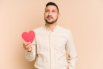 Adult latin man holding a red heart isolated dreaming of achieving goals and purposes
