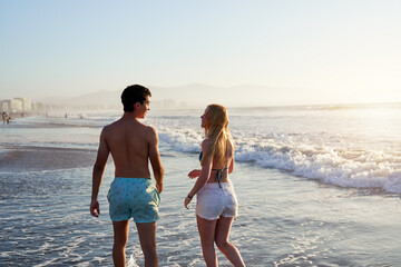two young argentinian latinos on the shore of the beach walking talking relaxed in bathing suits at...