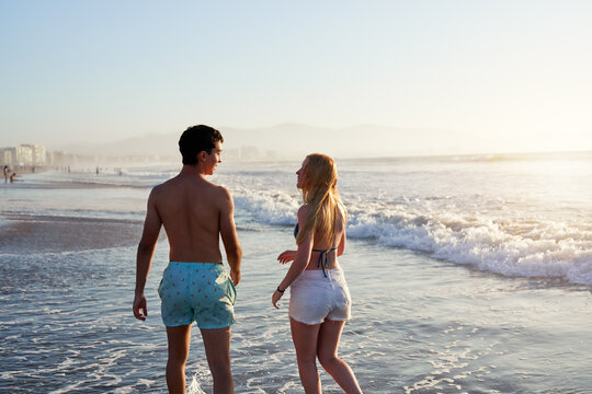 two young argentinian latinos on the shore of the beach walking talking relaxed in bathing suits at sunset