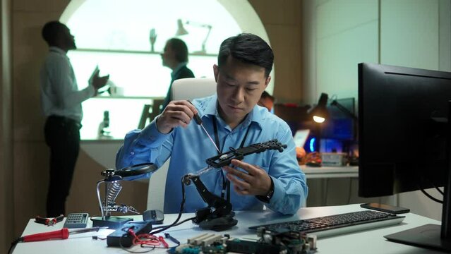 Portrait of busy smart asian male engineer building robotic hand using screwdriver working in robotics futuristic company. Attractive man technician developing prosthesis device in office.