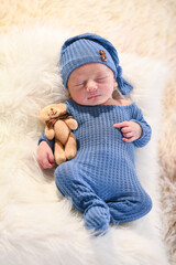 Cute newborn baby boy sleeping in pajamas, hat and teddy bear