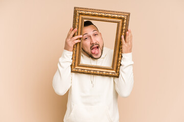 Adult latin man holding a vintage frame and smiling isolated