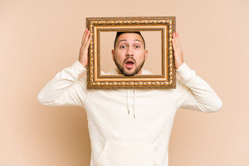 Adult latin man holding a vintage frame and smiling isolated