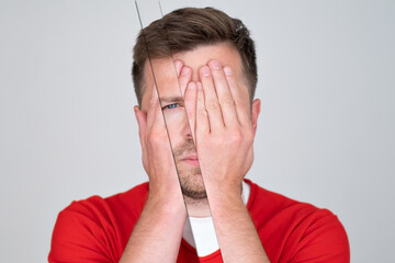 Young man covering his face by hand and looking at camera 