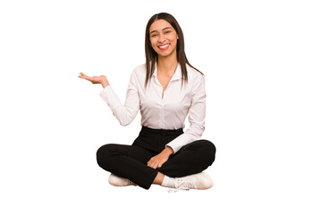 Young colombian woman sitting on the floor isolated showing a copy space on a palm and holding...