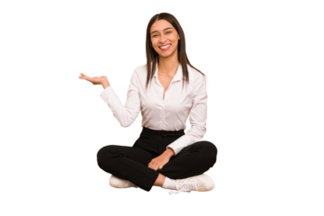 Young colombian woman sitting on the floor isolated showing a copy space on a palm and holding another hand on waist.